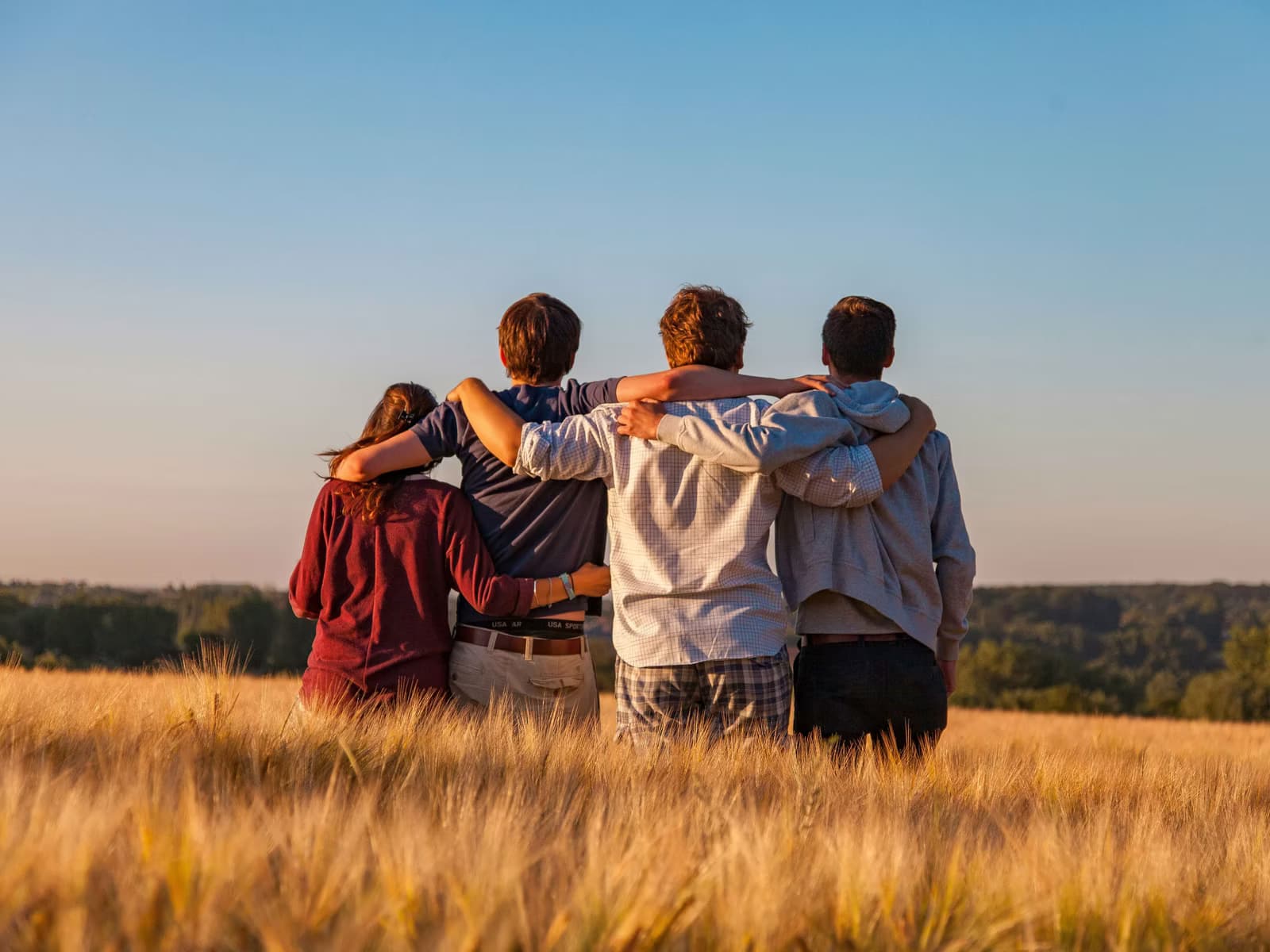 Vier Freundinnen und Freunde umarmen sich auf einem Feld bei Sonnenuntergang.