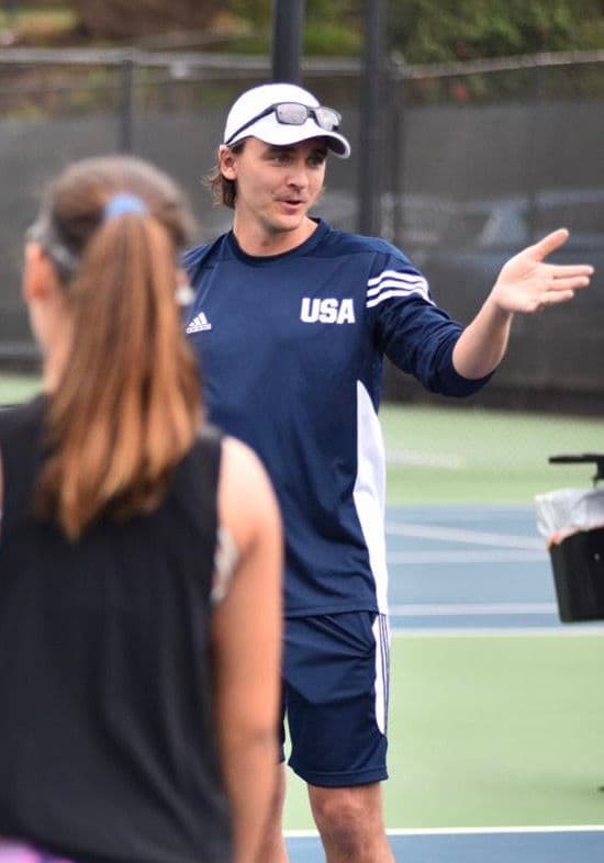 Coach explaining the next drill to an athlete on a tennis court.