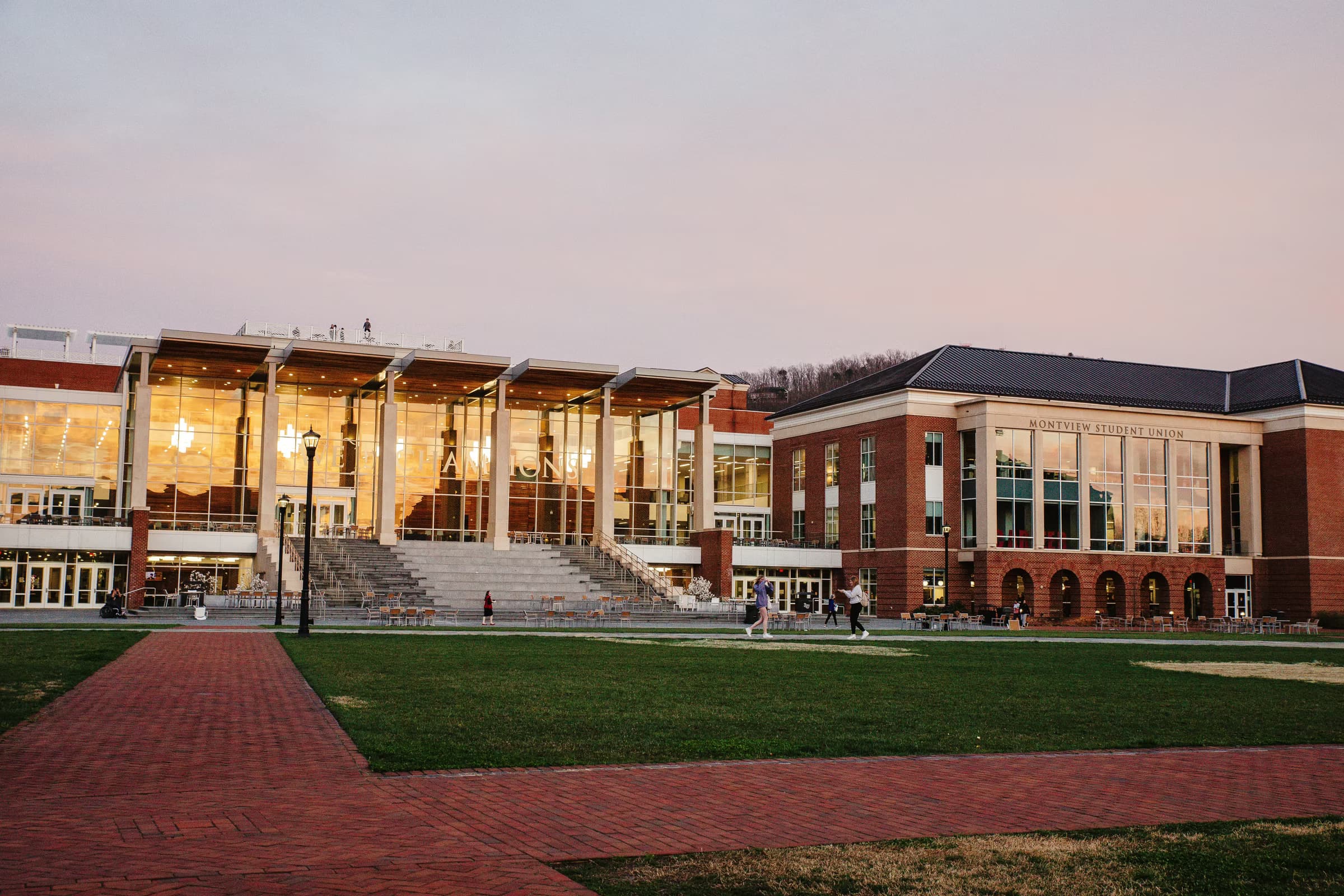 Modern university campus with glass façade, stairs and lawns at dusk.