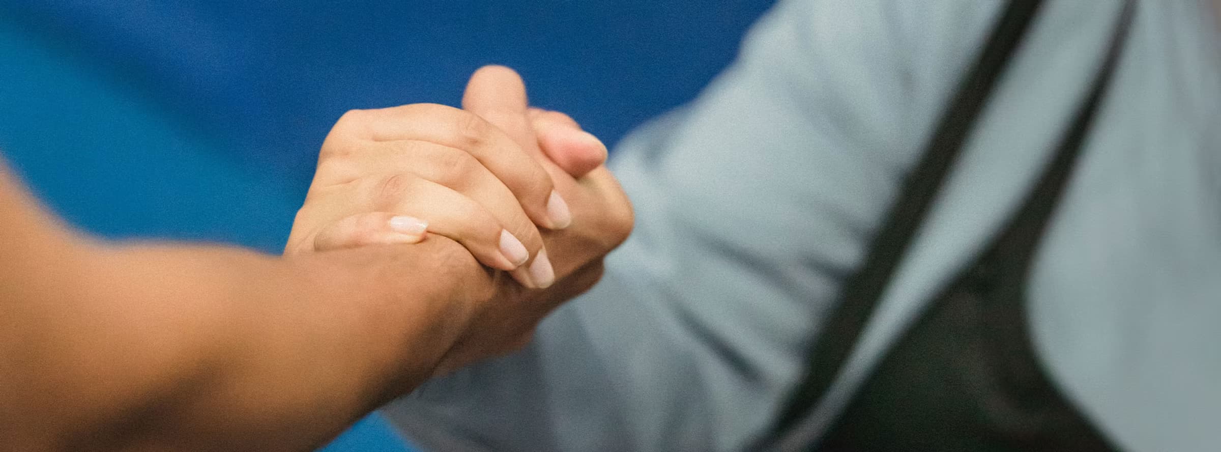 Close-up of a firm handshake against a soft blue background.