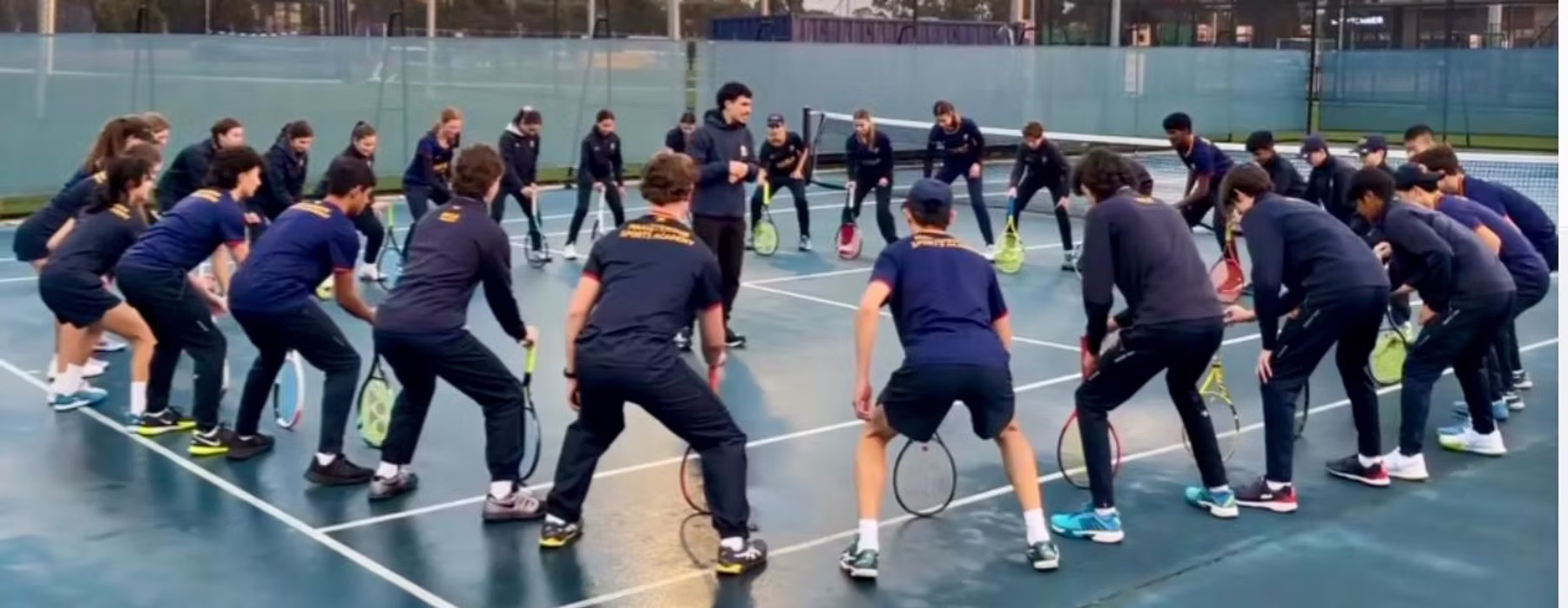 Tennis team in matching kits in a circle huddle on a blue hard court.